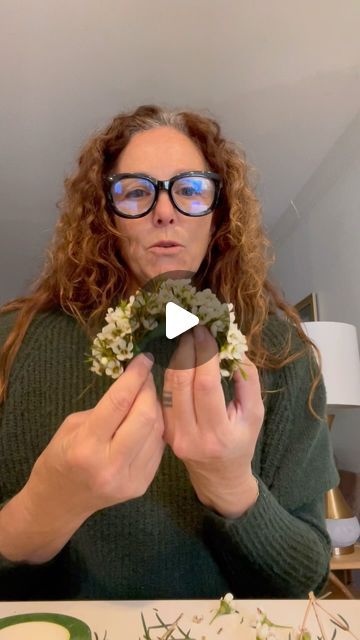 a woman in glasses is arranging flowers on a table with a video screen showing how to arrange the stems