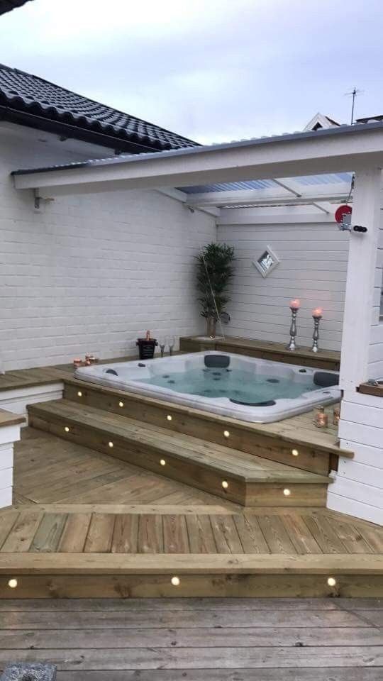 a hot tub sitting on top of a wooden deck next to a white building with lights