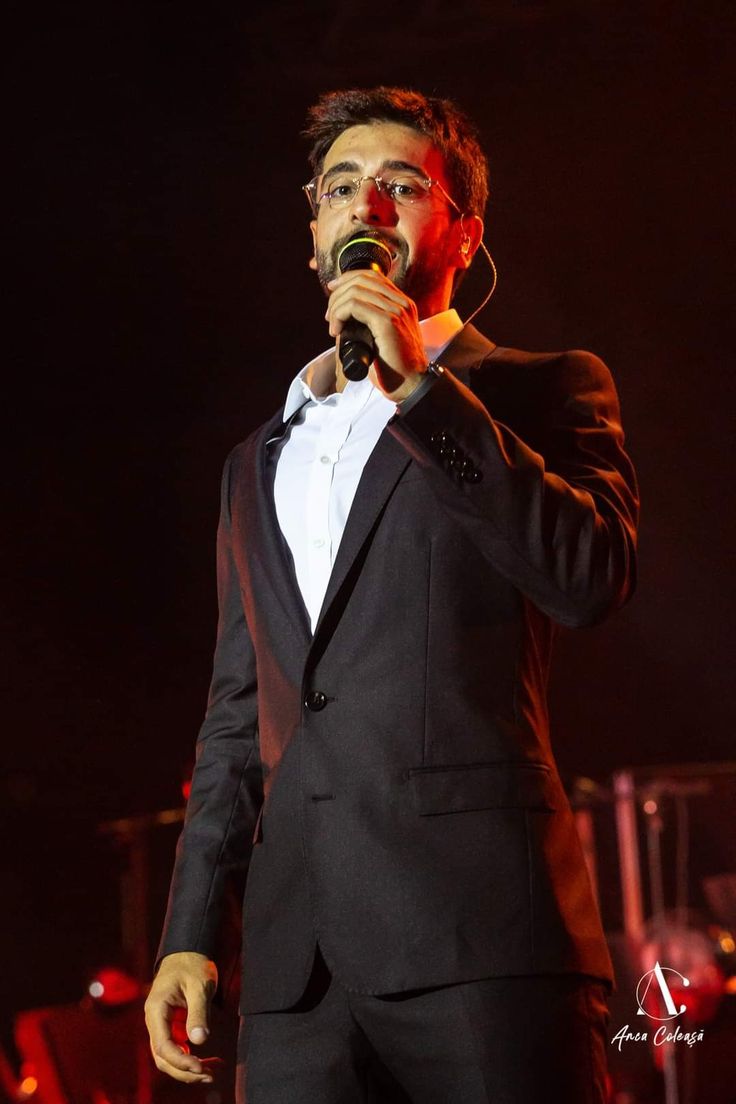 a man in a tuxedo singing into a microphone with his hands on his hips