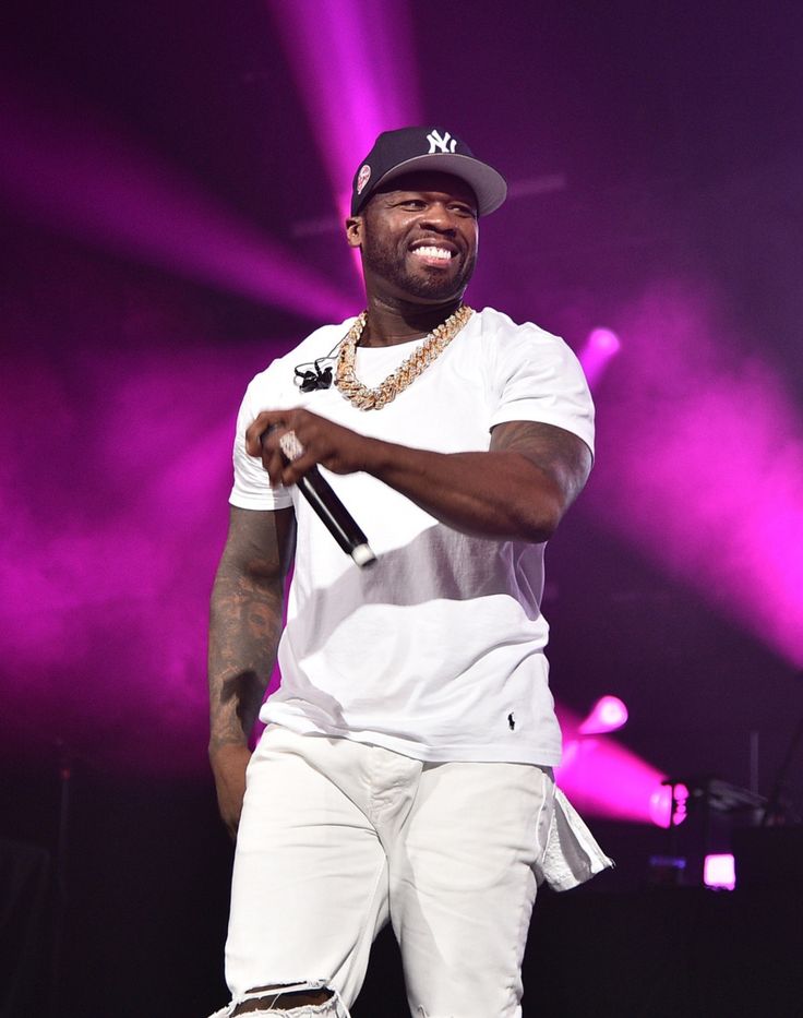 a man standing on top of a stage wearing white pants and a black baseball cap