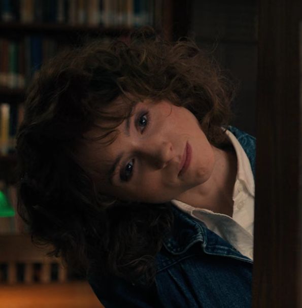 a woman with curly hair leaning against a book shelf