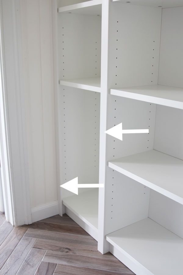 an empty white bookcase with two arrows pointing to the left and right ends, on a wood floor