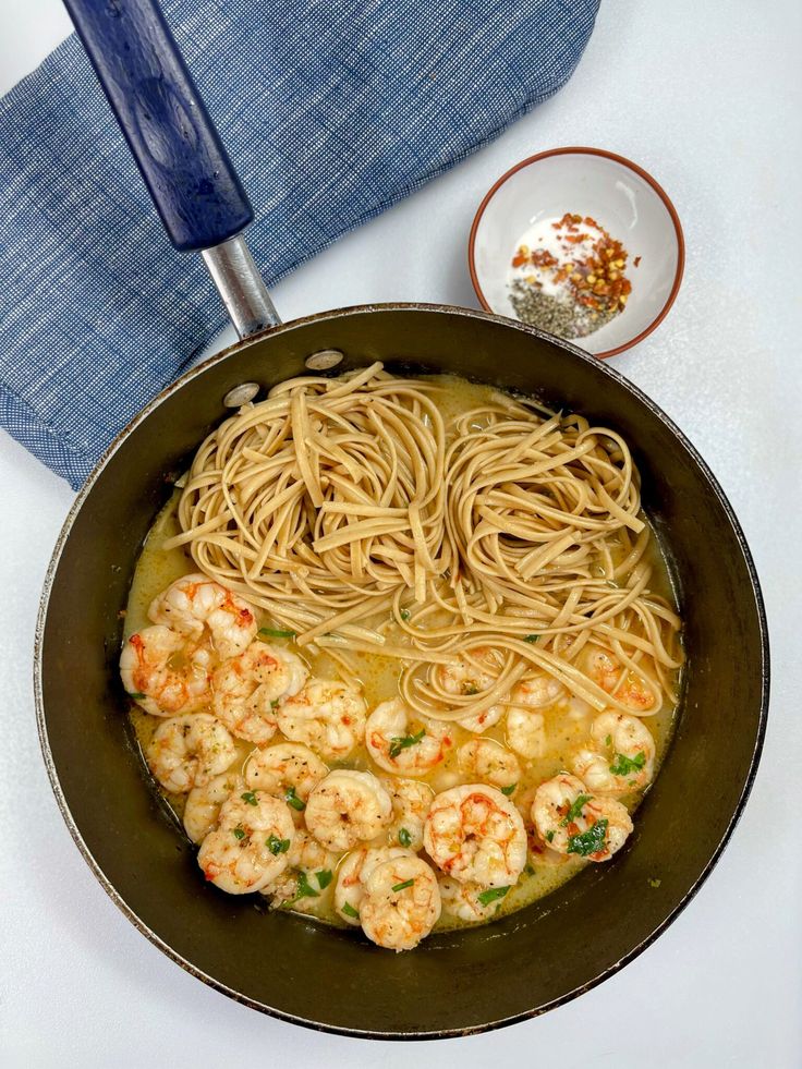 a pan filled with noodles and shrimp on top of a white counter next to a blue towel