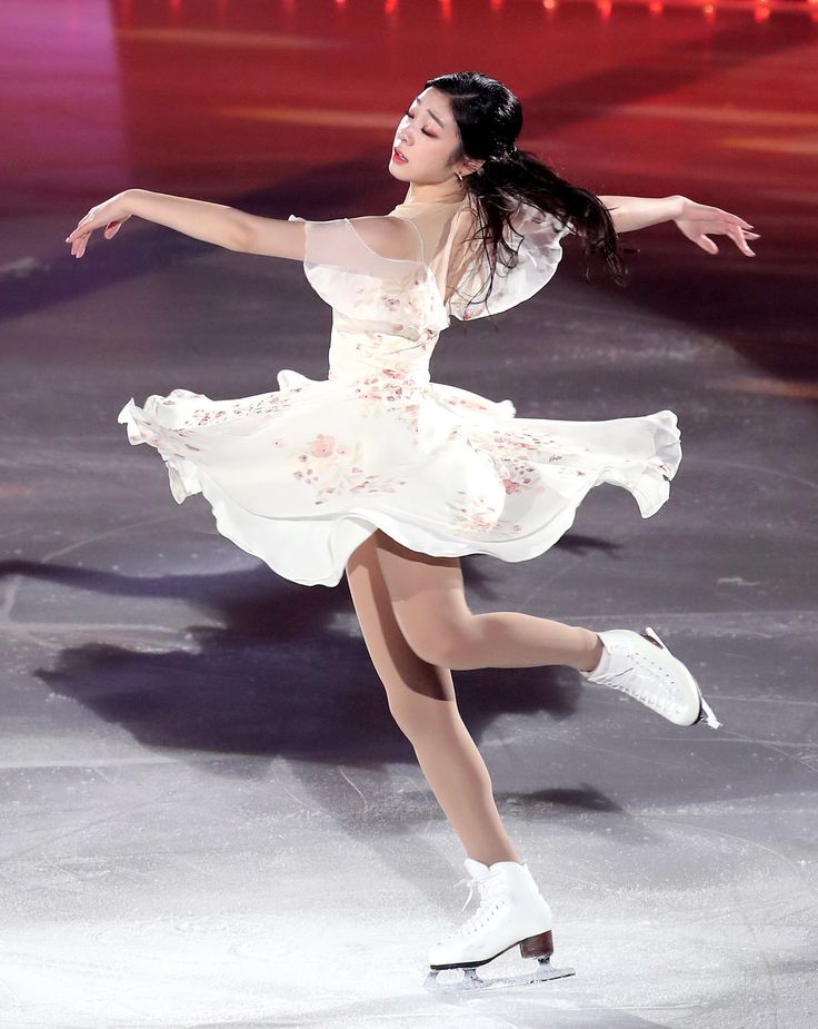 a woman in white skating on ice with her arms out and one leg bent forward