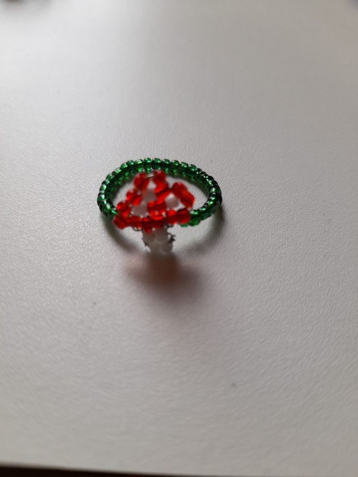 a red and green beaded ring sitting on top of a white table next to a pen