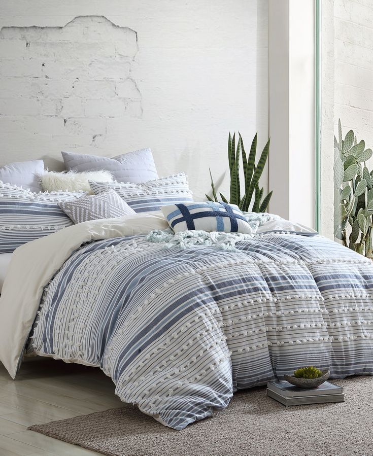 a bed with blue and white striped comforter next to a potted cacti