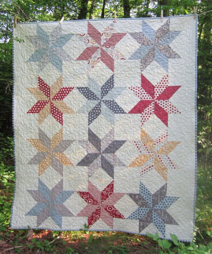 a quilt hanging from the side of a tree in front of some trees and grass