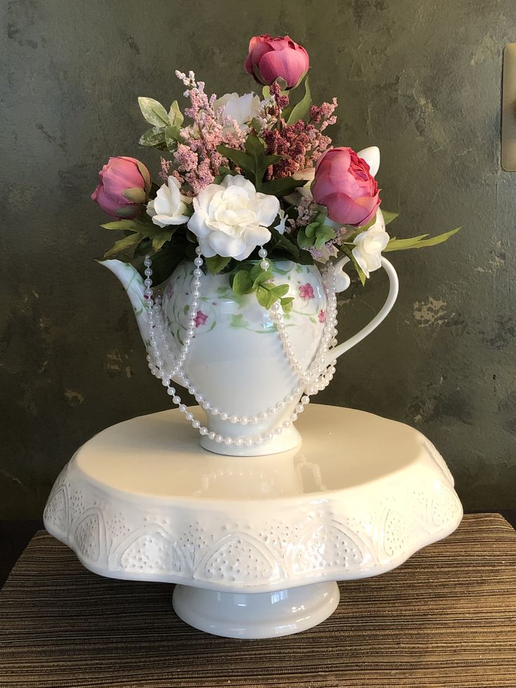 a white vase with pink and white flowers in it sitting on a cake platter