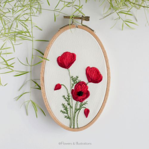 the embroidery pattern shows three red flowers on a white background with green grass in the foreground