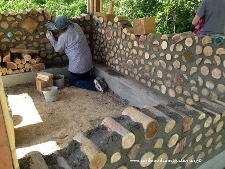 two men are working on some kind of wall made out of tree trunks and logs