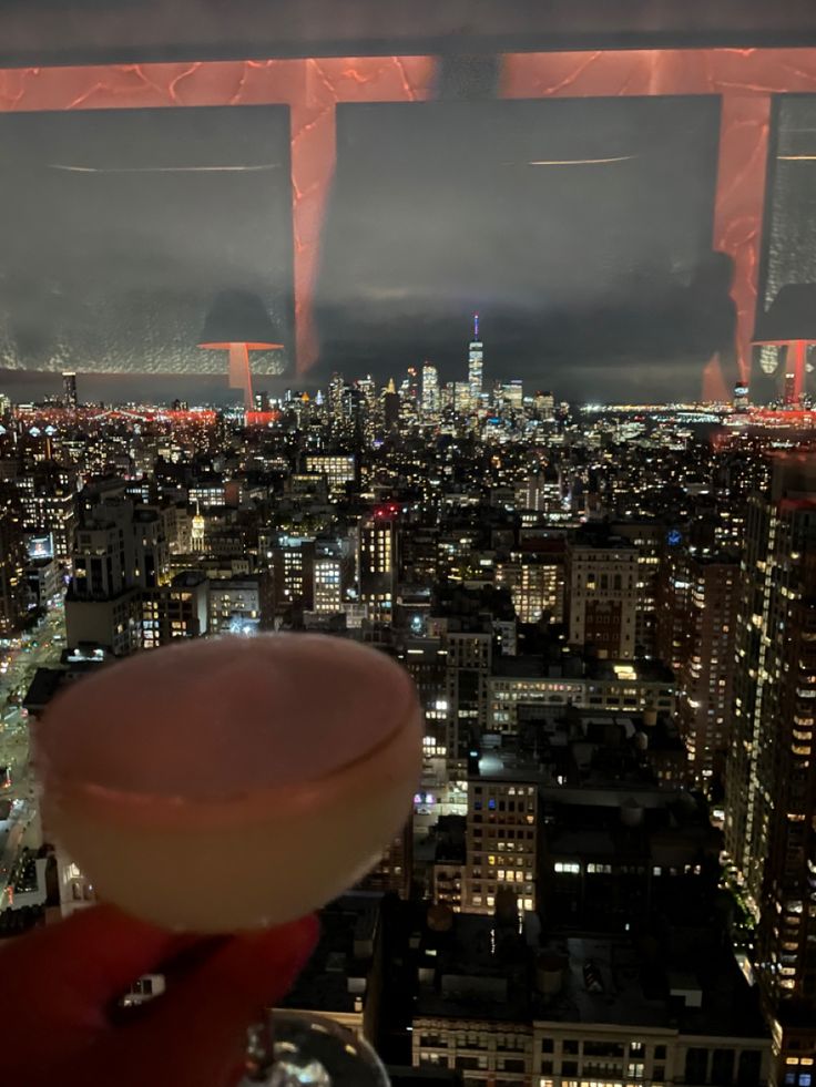 a person holding up a wine glass in front of a cityscape at night