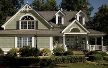 a large green house with white trim on the front and side windows, surrounded by greenery