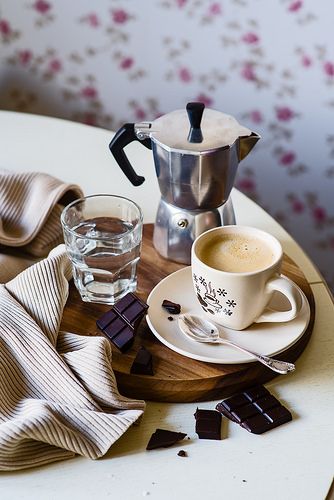 a wooden tray topped with a cup of coffee next to a glass and saucer