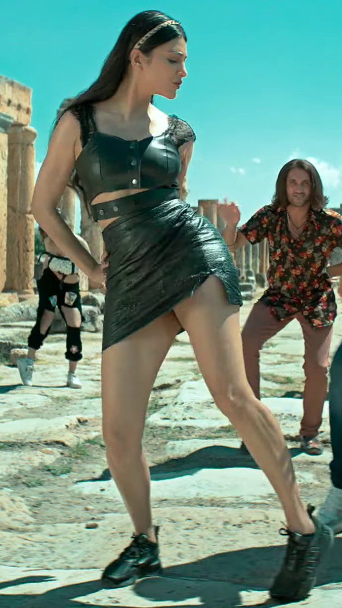 two women are dancing in the middle of a desert with other people behind them and one is wearing a black leather skirt