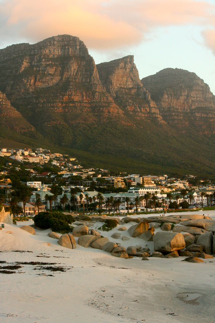 the beach is covered in white sand and has mountains in the background with houses on it