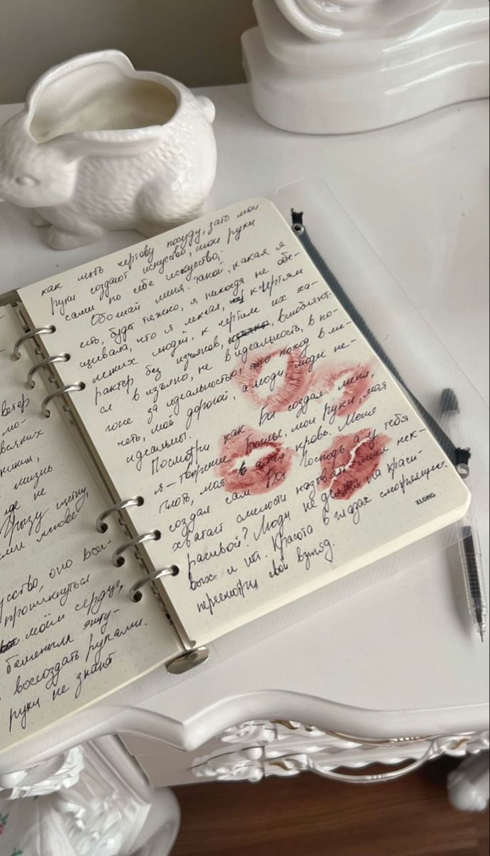 an open notebook with writing on it sitting on a table next to a white vase