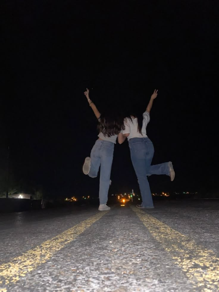 two people jumping in the air with their arms up on a street at night time