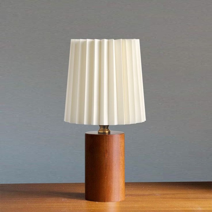 a wooden table with a white lamp on it and a gray wall in the background