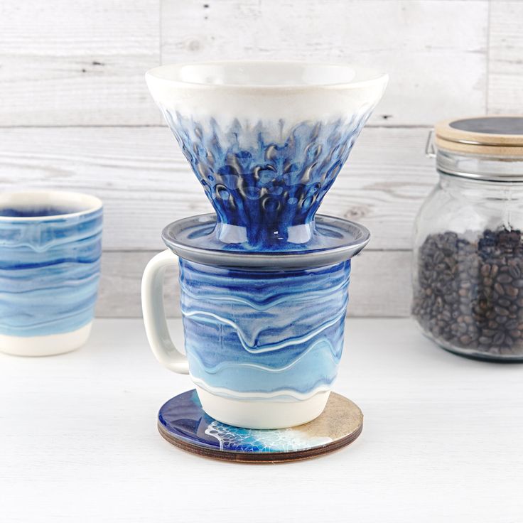 blue and white cups sitting on top of each other next to a jar filled with coffee beans