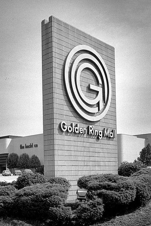 the golden ring mall sign is shown in black and white, with bushes around it