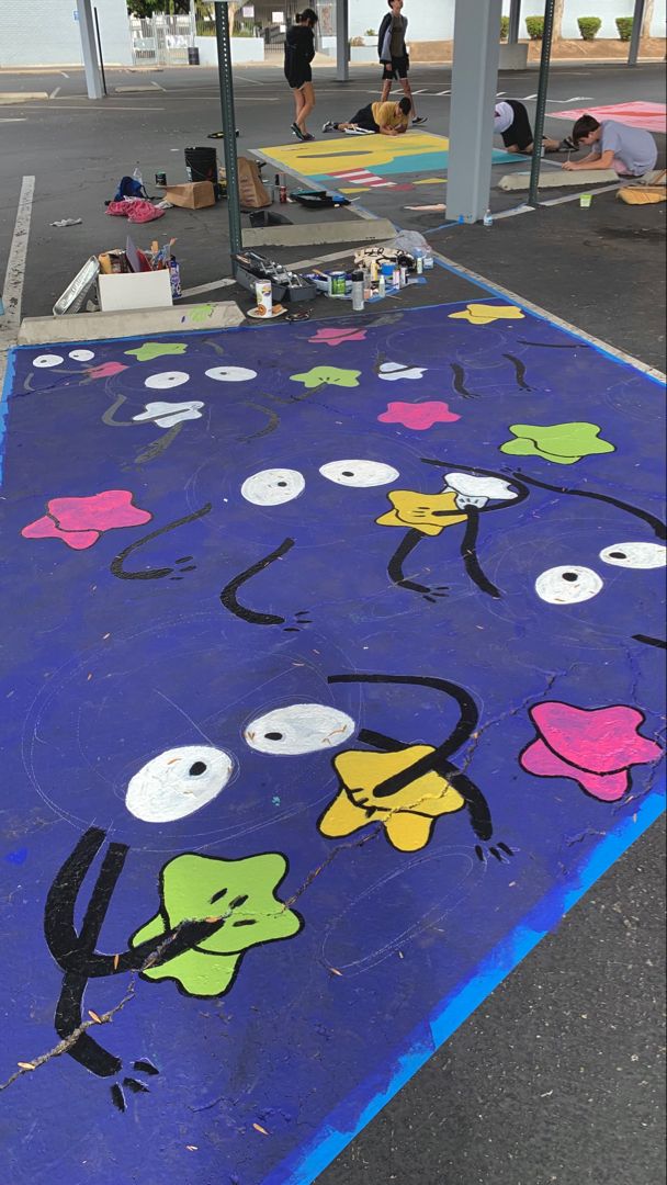 people are painting on the ground in front of a gas station with cartoon characters painted on it