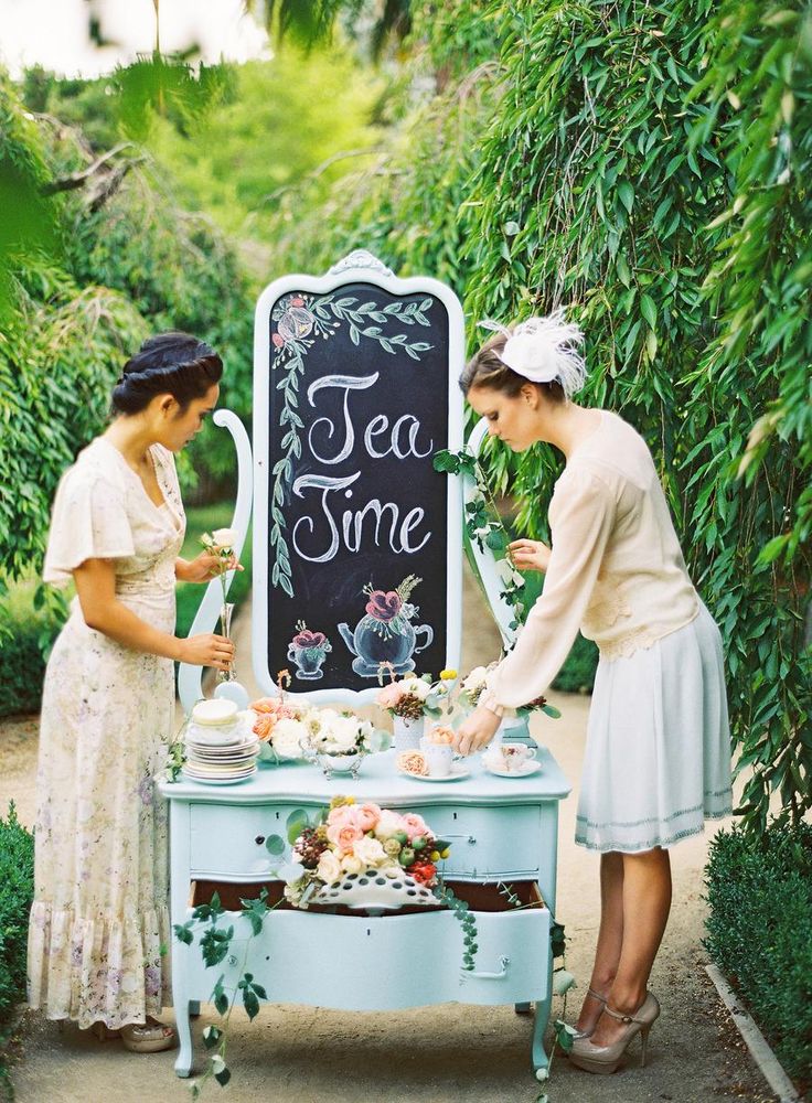 two women standing in front of a sign with tea time written on it