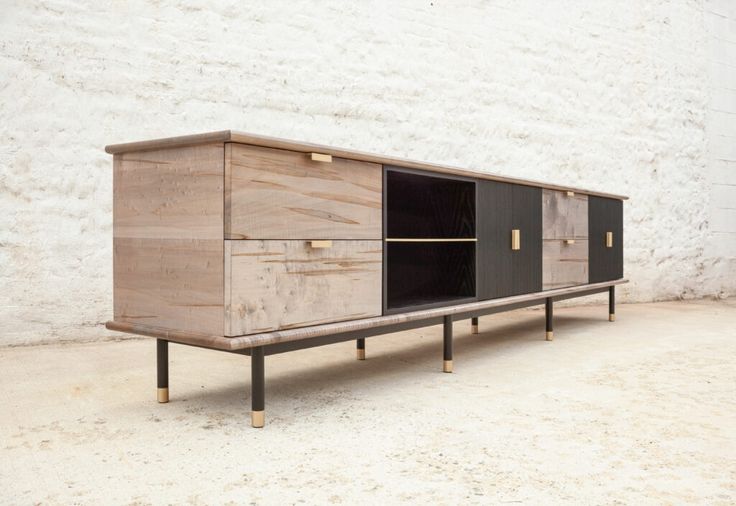 a wooden sideboard with black doors and gold handles on the bottom, against a white brick wall