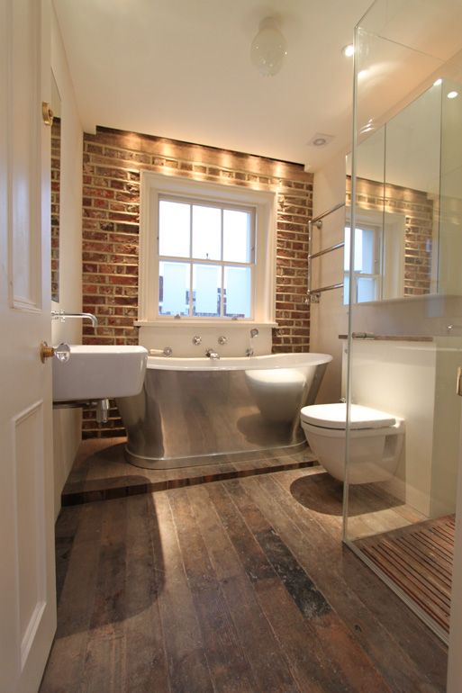 a bathroom with a tub, toilet and sink in it's center area next to a brick wall