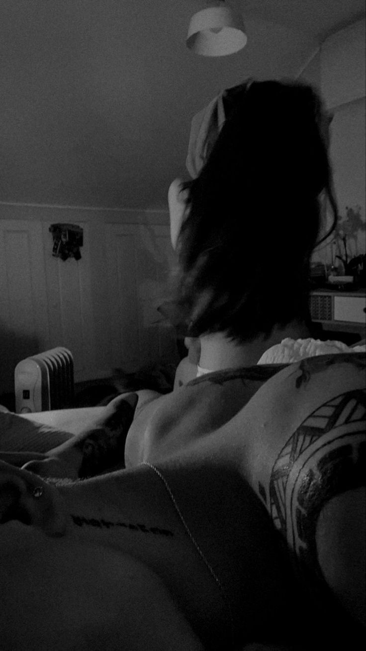 black and white photograph of a woman with tattoos on her back laying down in bed