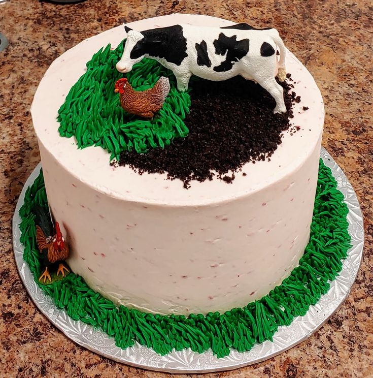 there is a cake decorated with grass and cows on the top, sitting on a table