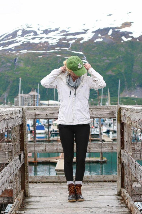 a woman is standing on a dock with her head in her hands and wearing a green hat