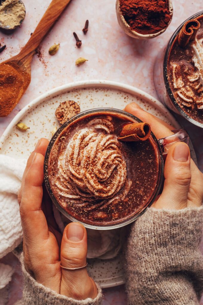 two hands holding a cup of hot chocolate with cinnamon sprinkles on top