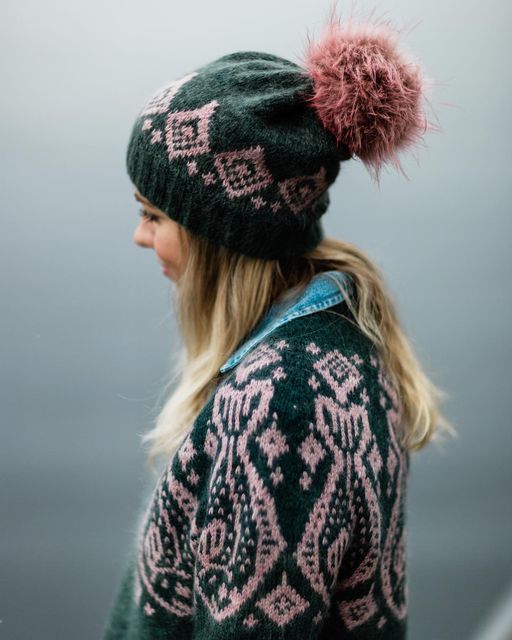 a woman wearing a green sweater and pink pom - pom hat