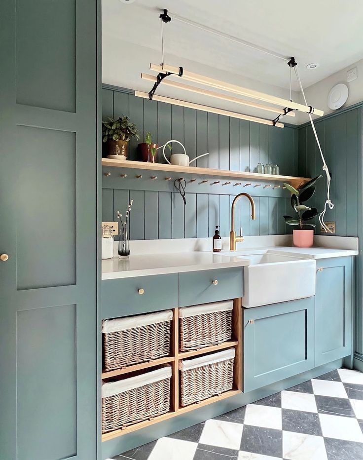 a kitchen with blue cabinets and white checkered flooring on the walls, an open shelving unit above the sink is filled with wicker baskets