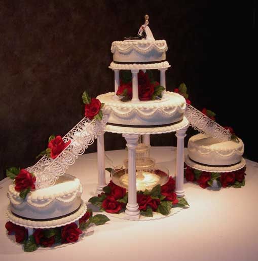 three tiered wedding cake with red roses on the table