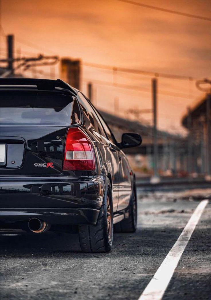 the back end of a black car parked in front of a train track at sunset