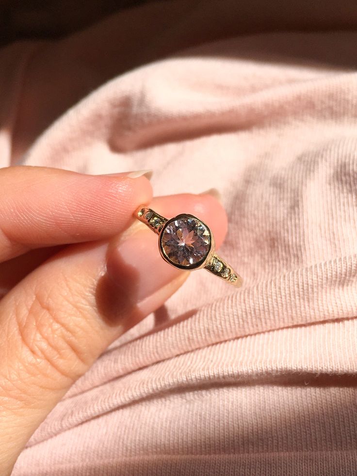 a woman's hand is holding a ring with a pink diamond on it and gold