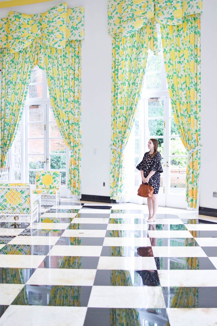 a woman is standing in the middle of a room with checkered floor and yellow curtains