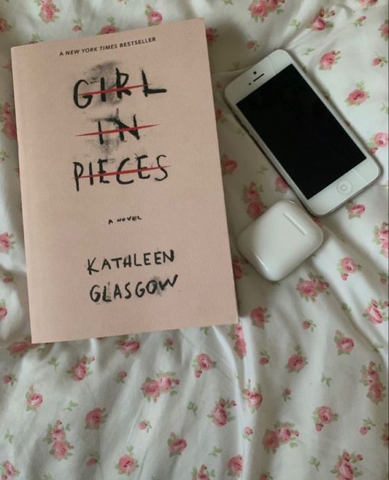 the book girl in pieces is next to an iphone and headphones on a bed