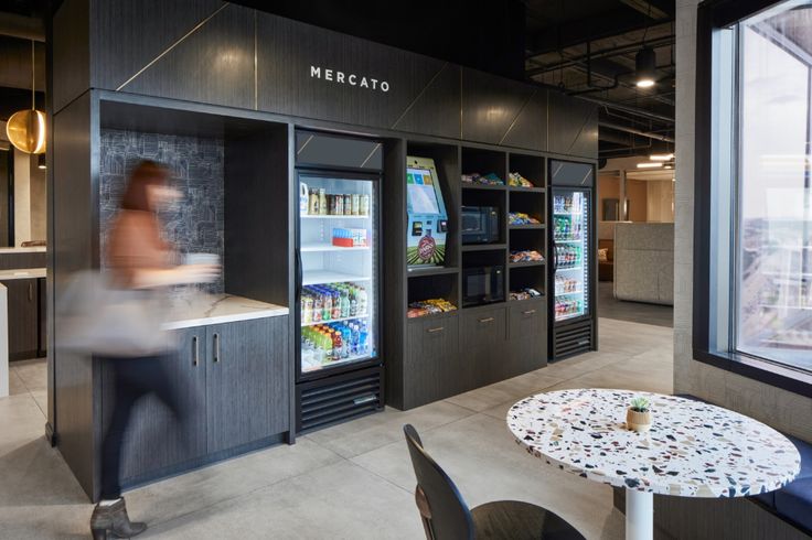 a woman is walking past a vending machine in a store with lots of shelves