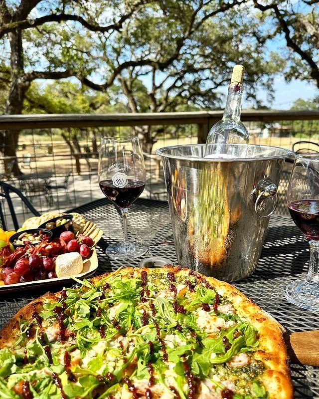 two pizzas on a table with glasses of wine and grapes in the foreground