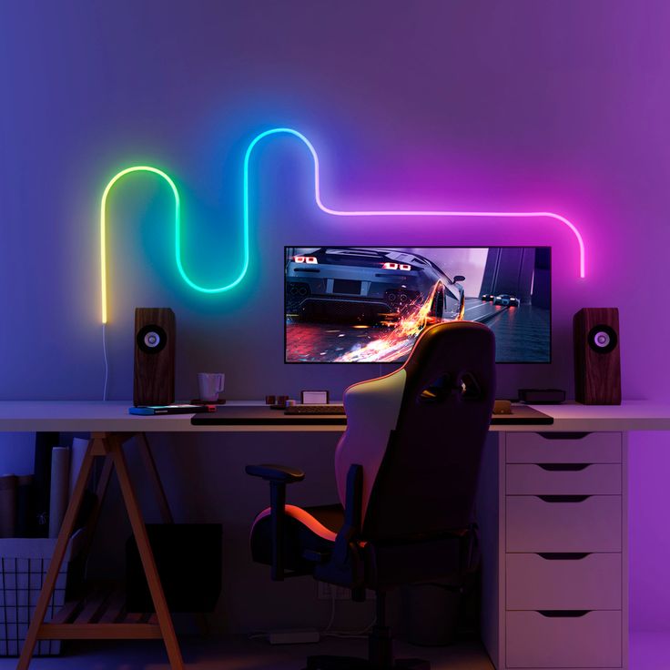 a computer desk with a monitor and speakers on it in front of a neon colored wall