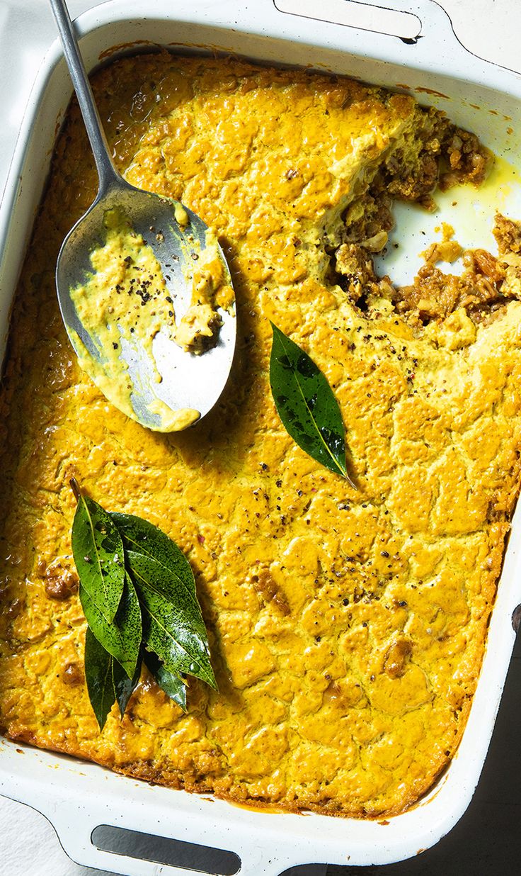 a casserole dish with green leaves on top and a spoon in the casserole