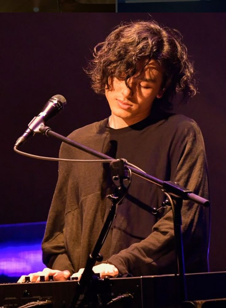 a man standing in front of a microphone on top of a keyboard with his eyes closed