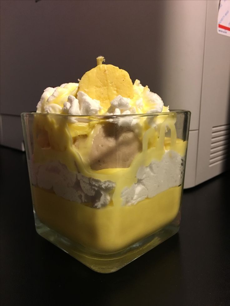 a glass dish filled with yellow and white dessert on top of a black table next to a microwave