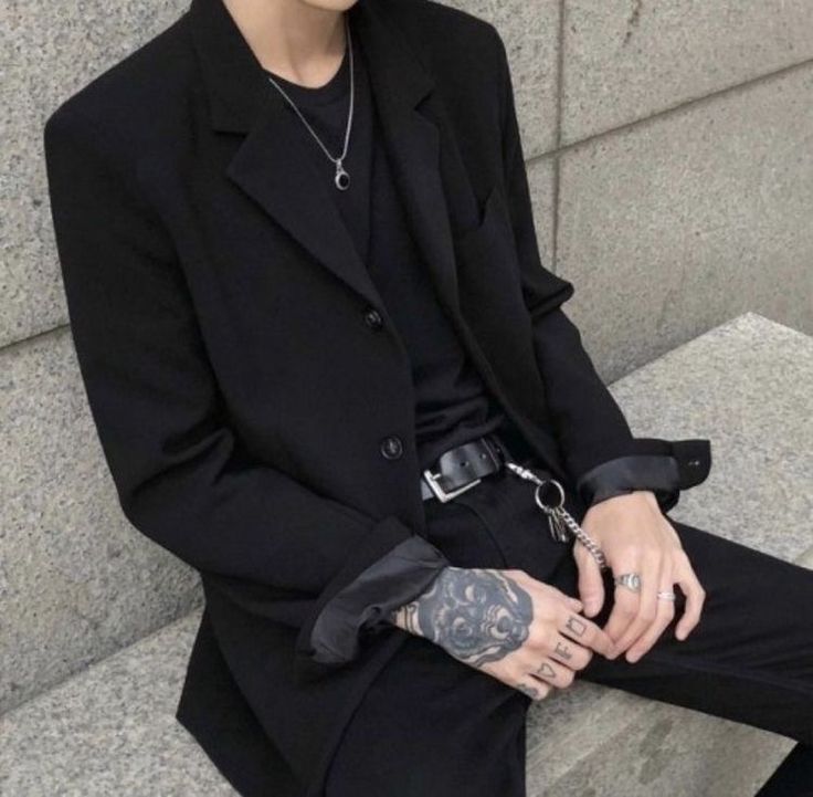 a man with tattoos sitting on the steps wearing a black suit and tie, holding his hands in his pockets