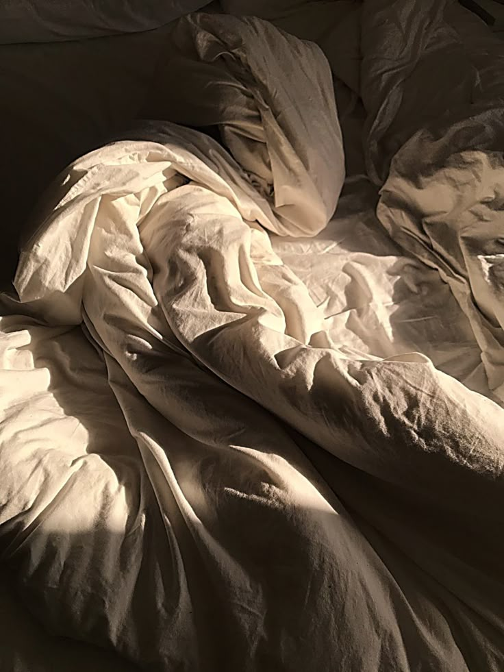 an unmade bed with sheets and pillows on top of it, in the sunlight