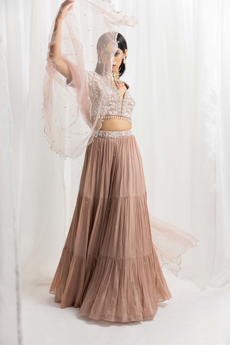 Editor's Note The embellished choli is paired with a tiered skirt featuring an embellished waistbelt. The outfit is completed with a net scalloped dupatta, creating an elegant and sophisticated look. Fabric: Choli: georgette, skirt: chiffon, dupatta: net, satin lining Color: Dusty pink Components: Lehenga, blouse and dupatta Occasion: Engagement, festive and wedding guest Disclaimer: Product color may slightly vary due to photographic lighting sources or your monitor setting. Care: Dry clean onl Organza Lehenga With Tiered Skirt For Party, Organza Tiered Lehenga For Party, Organza Tiered Skirt Lehenga For Party, Designer Georgette Party Wear Skirt Set, Designer Georgette Skirt Set For Party Wear, Anarkali Skirt Set With Sheer Dupatta, Elegant Georgette Skirt Set For Reception, Elegant Party Sharara With Tiered Skirt, Elegant Tiered Sharara For Party