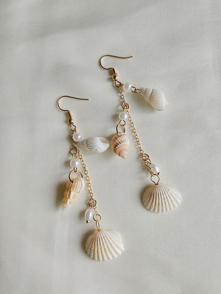 three seashells hanging from gold chains on a white sheet with pearls and beads