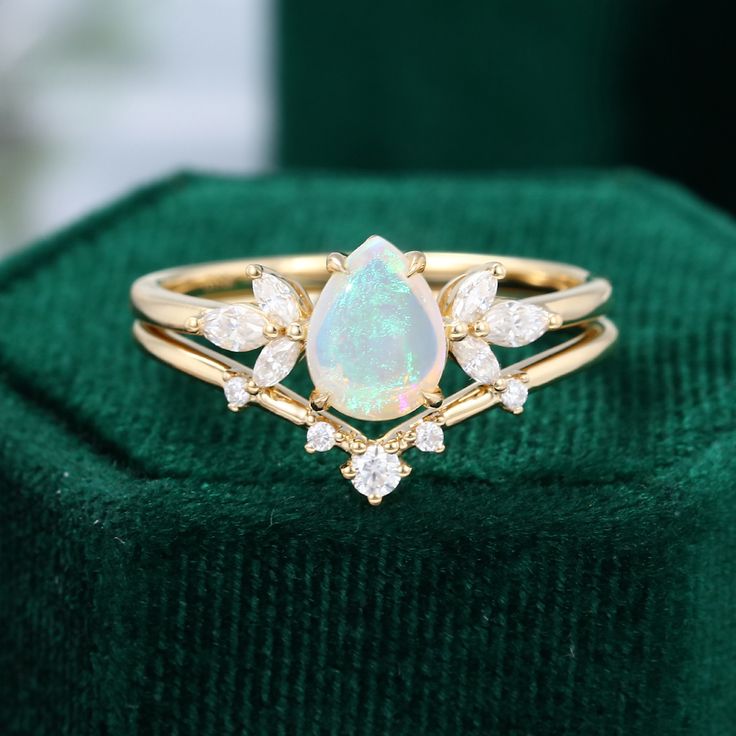 an opal and diamond ring sits on top of a green velvet box